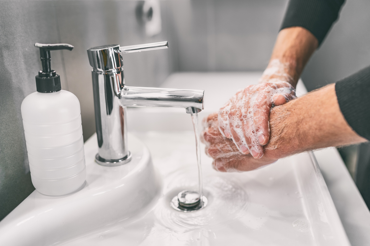 Adult washing hands with a thick lather of soap above a white sink with a white soap dispenser. 